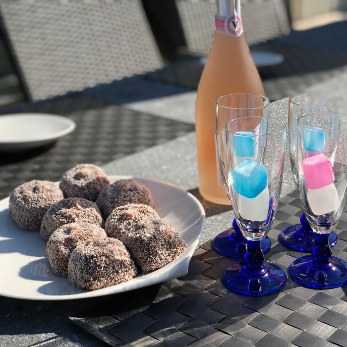 A bottle of sparkling rose wine, four champagne glasses and a plate of chocolate-coated marshmallow treats