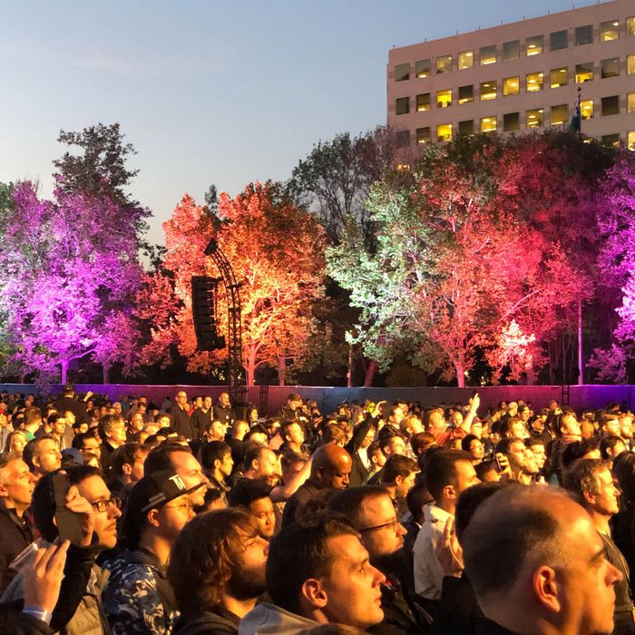 A crowd standing in front of the stage at the WWDC18 Bash with trees lit up in difference colors in the background