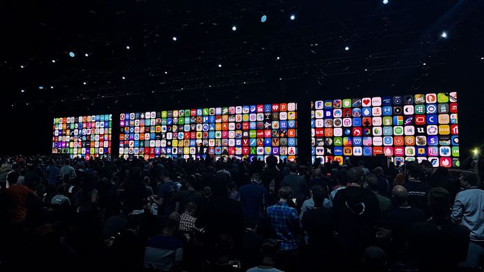 A crowd of developers waiting for the WWDC keynote to start with lots of app icons on the screens